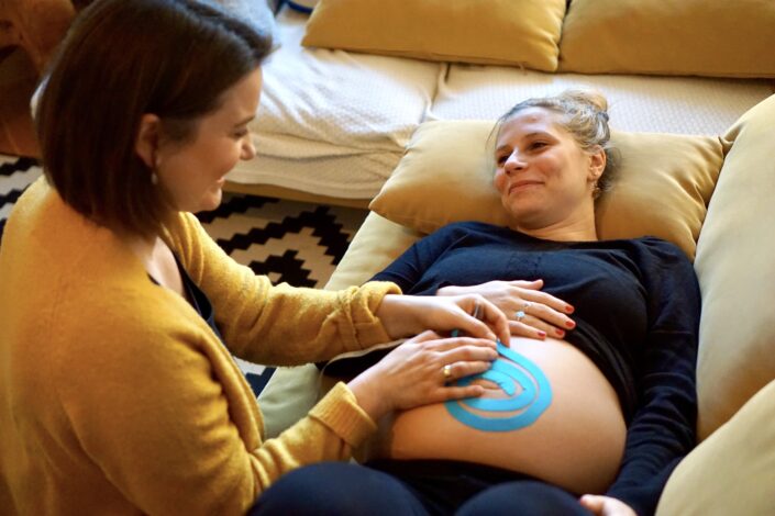Hebamme beim Taping des Babybauches einer Patientin